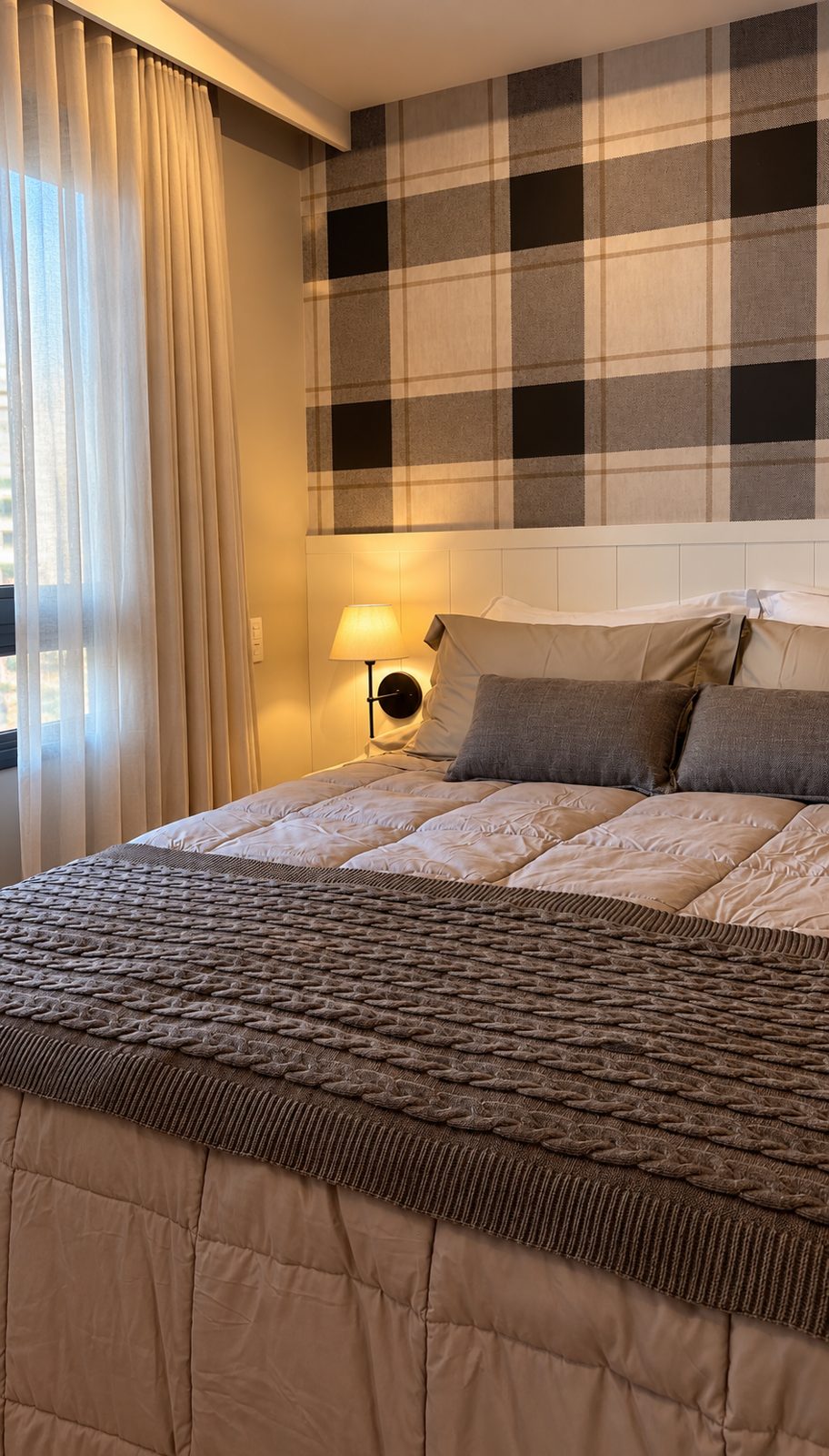 Cama con papel pintado a cuadros, cabecero blanco panelado, aplique y cortinas livianas
