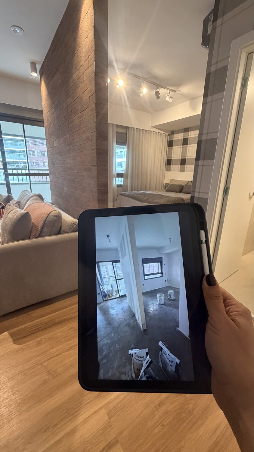 Fotografía del apartamento terminado con pared de ladrillo y, en la pantalla de una tableta, la misma sala durante la obra