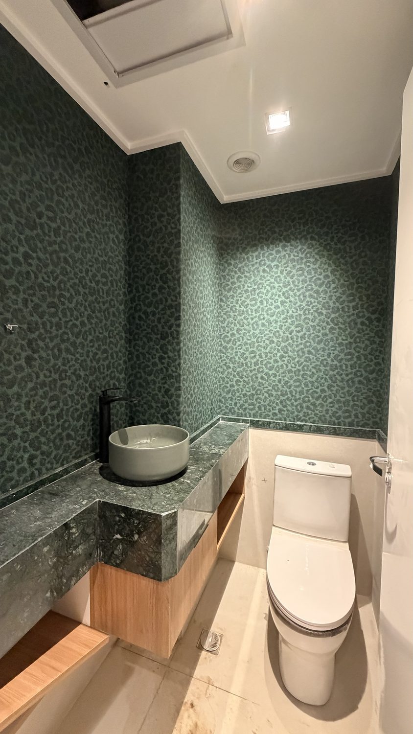 Lavabo con papel pintado verde, encimera de mármol verde y mueble de madera en etapa de acabado