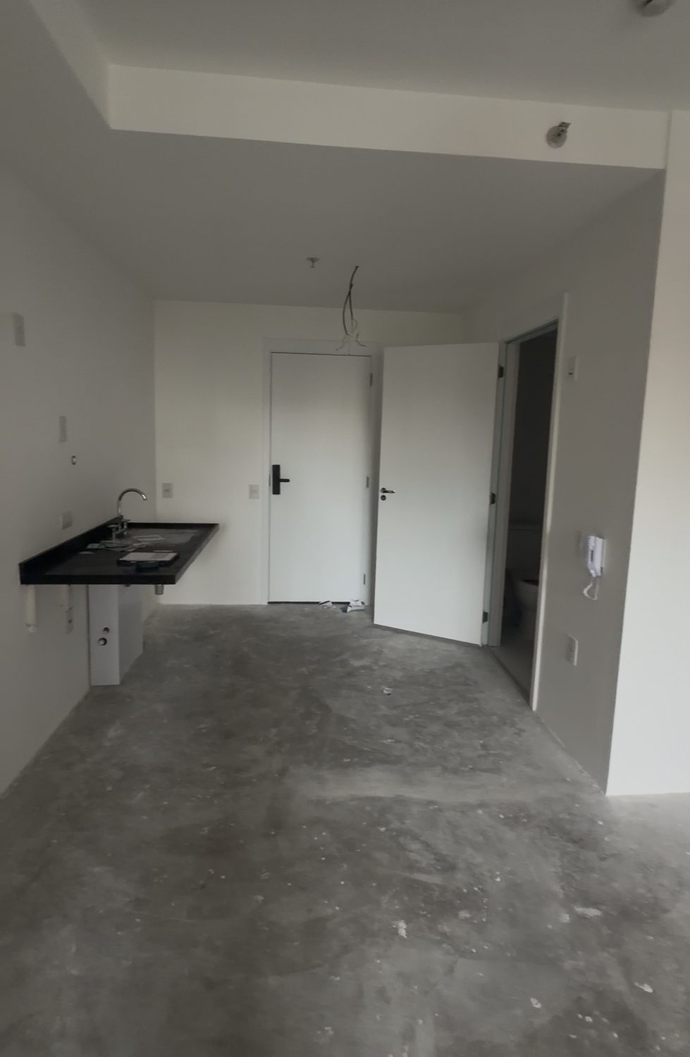 Apartamento en obra con contrapiso a la vista, mesada en negro con fregadero y puerta de acceso