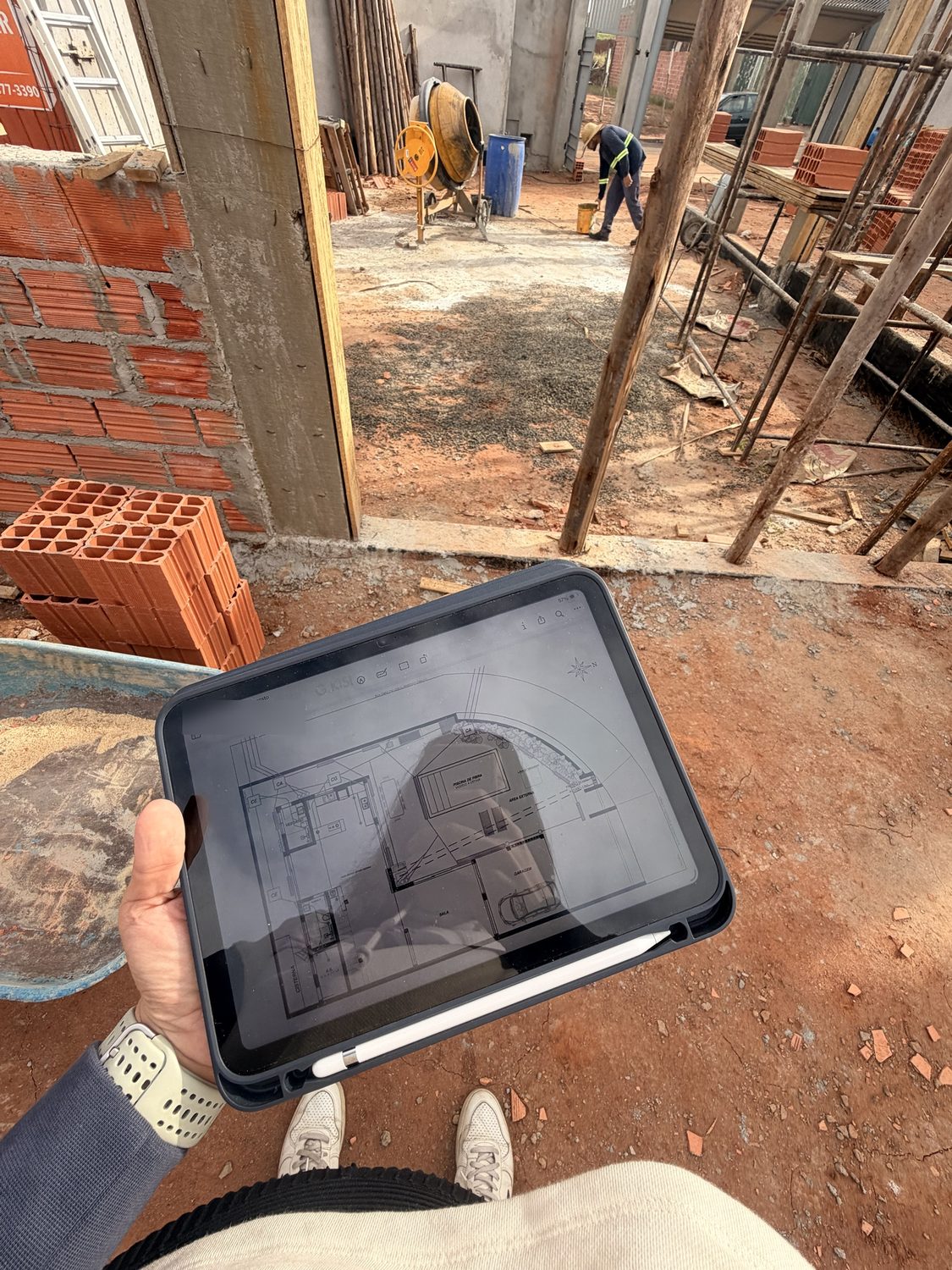 Visita de obra con el plano de distribución abierto en una tableta frente a la alvenaría y el encofrado